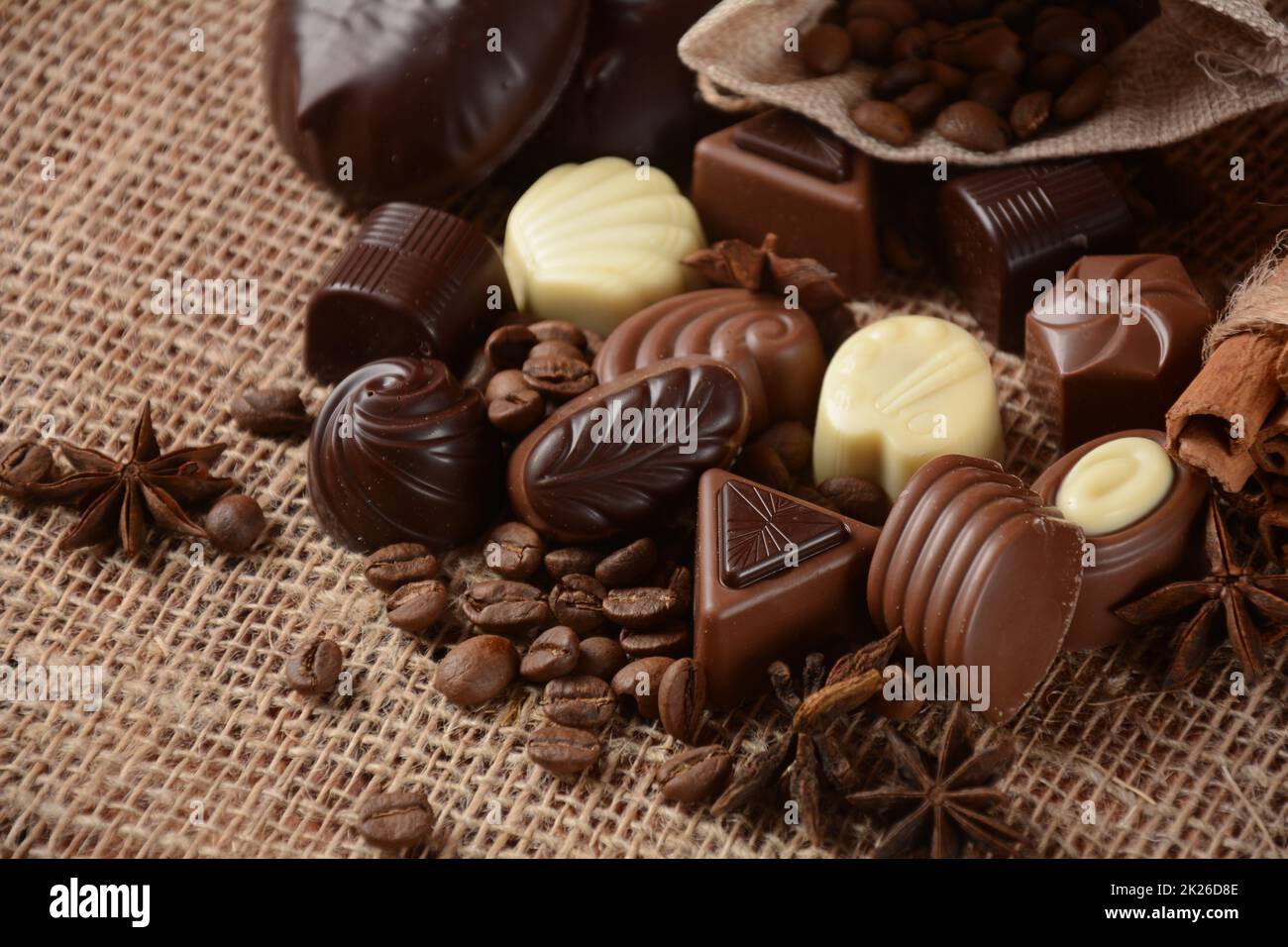 Assortment of dark, white and milk chocolate sweets, zefir (zephyr). Chocolate and coffee beans on rustic wooden sacking background. Spices, cinnamon. Chocolates background. Stock Photo