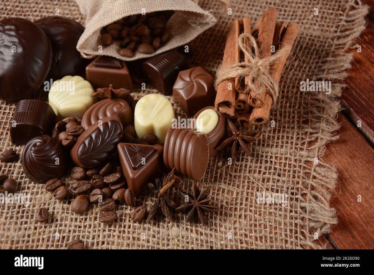Assortment of dark, white and milk chocolate sweets, zefir (zephyr). Chocolate and coffee beans on rustic wooden sacking background. Spices, cinnamon. Chocolates background. Stock Photo