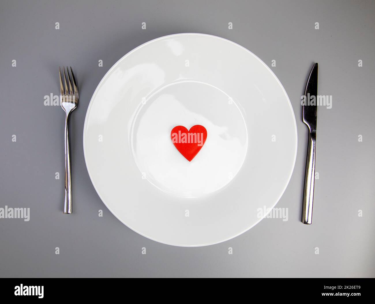 White plate with, fork and knife, red heart on grey background, flat lay. Valentine's day or medical health concept top view Stock Photo