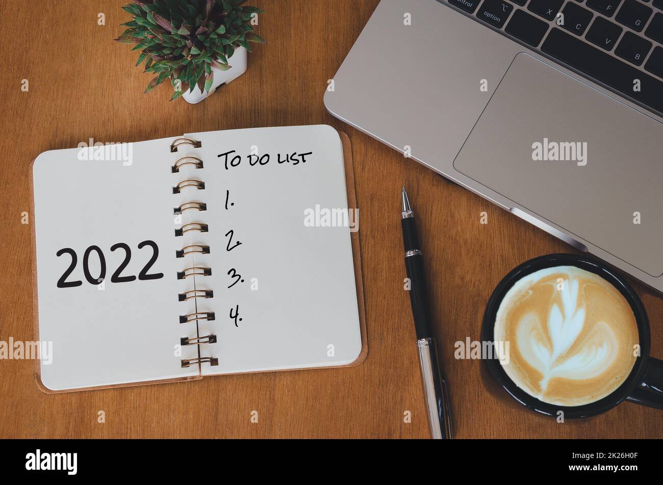 computer laptop Notebook and pen and cactus with coffee cup on desk.Top view to do list 2022 new year. Stock Photo