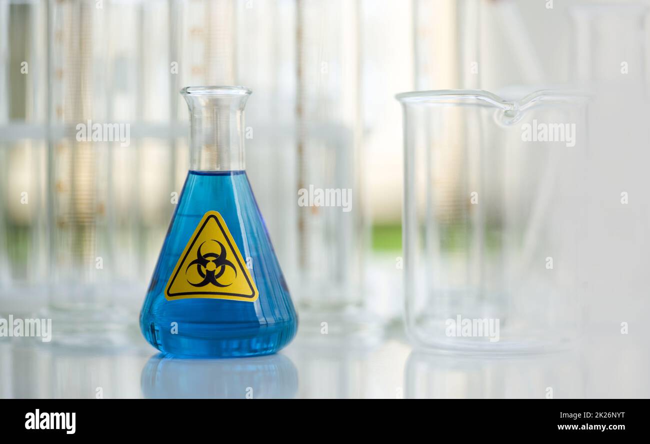 Erlenmeyer Flask contains blue liquid chemicals on white laboratory table. Stock Photo