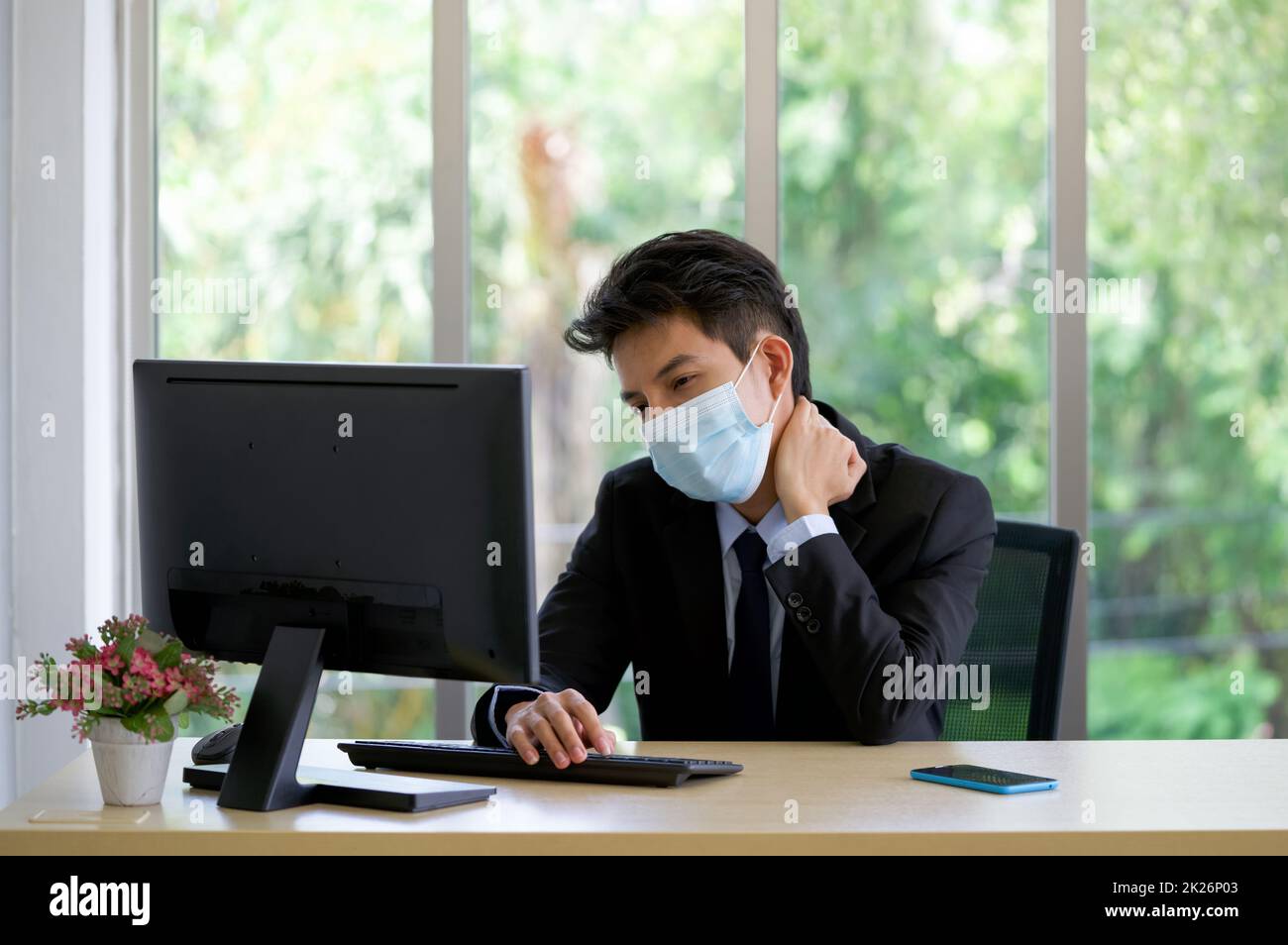 Young asian businessman in suit and face mask grab the neck with his hand. To alleviate pain from prolonged computer use. Stock Photo
