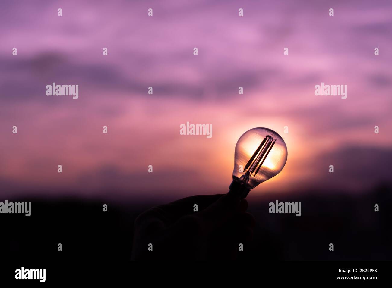 Silhouette of a light bulb held by a person's hand in a purple sunset sky that leaves speechless Stock Photo