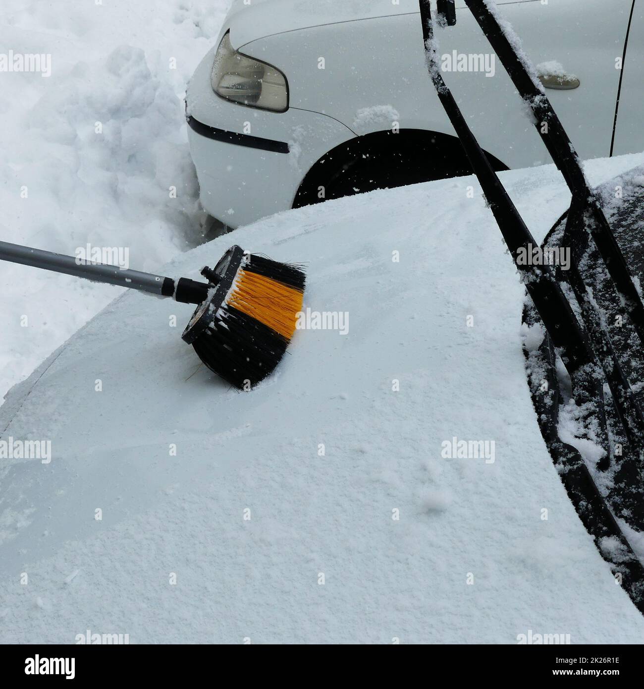 cleaning the snow accumulated on the car with a brush, snow falling on