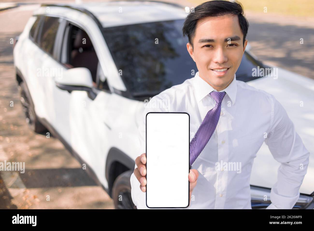 young smiling business man showing mobile phone with white empty screen and standing before the car Stock Photo