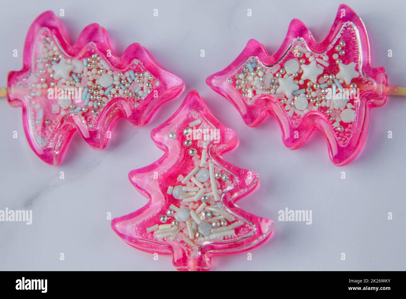 Three pink Christmas trees lollipops on a wooden leg with powder inside lie on a light marble background Stock Photo