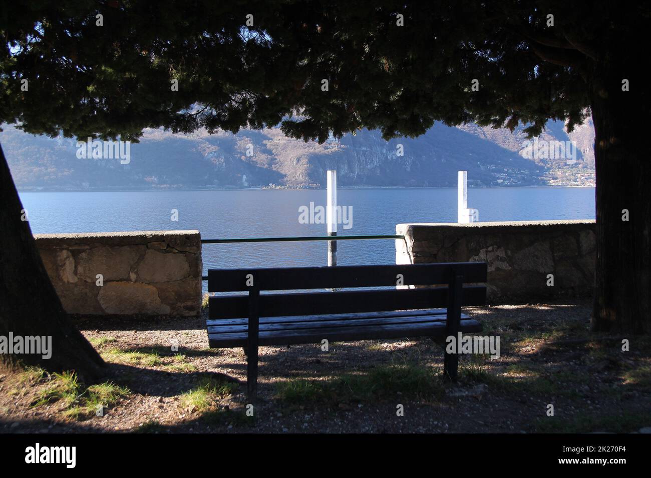 A bench under the trees looking at the traditional docking and Como Lake Stock Photo