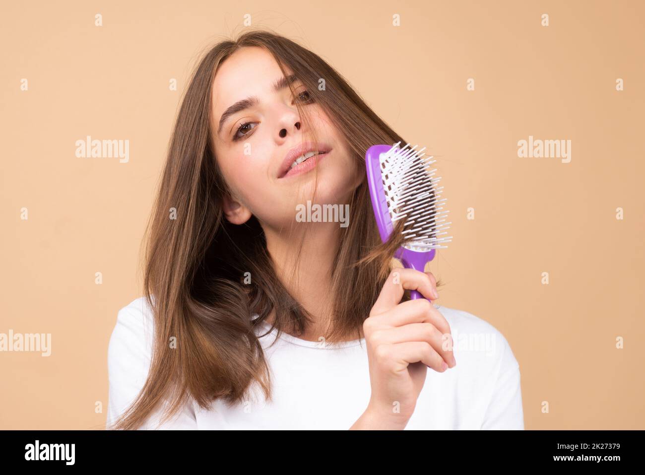 Smiling woman brushing hair with comb. Beautiful girl combing long hair with hairbrush. Stock Photo