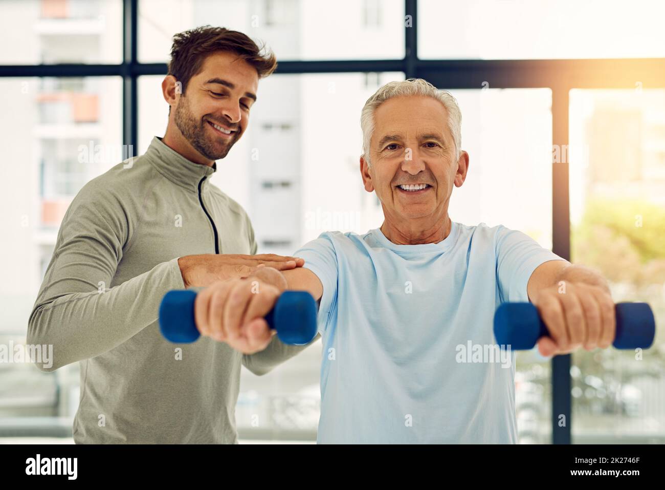 Seniors can be strong too. Portrait of a friendly physiotherapist helping his senior patient work out with weights. Stock Photo