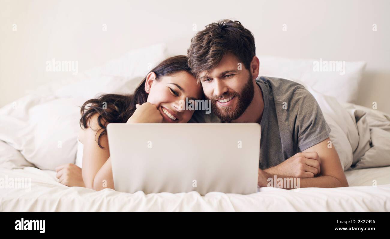 Save some time everyday to connect. Shot of a happy young couple using a laptop while relaxing on the bed at home. Stock Photo