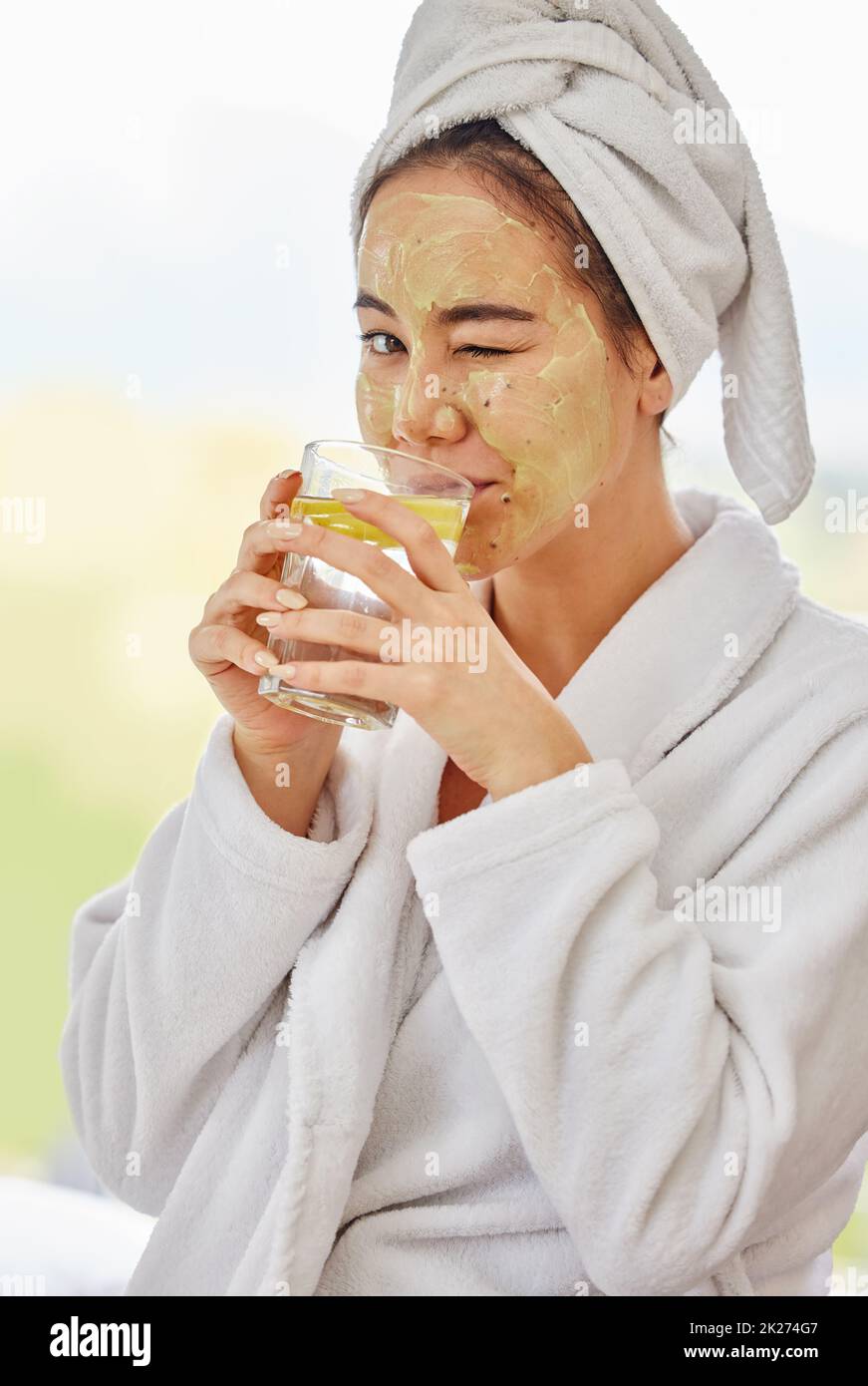 Cleanse yourself from the inside out. Shot of a young woman drinking water while doing a facial beauty treatment at home. Stock Photo