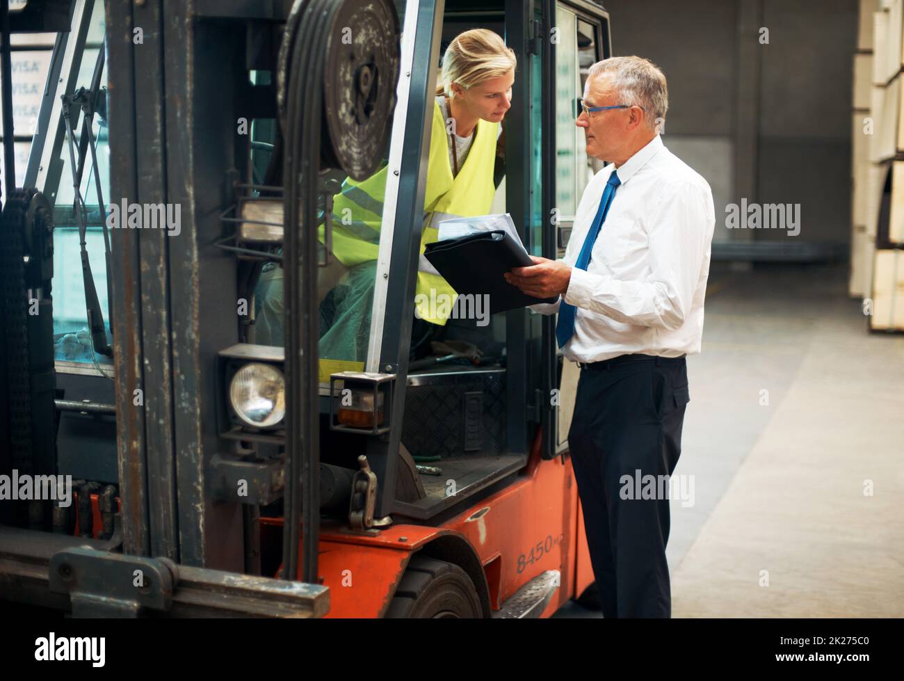 Listen and learn from the best. A manager giving orders to an employee who's sitting on a forklift.. Stock Photo