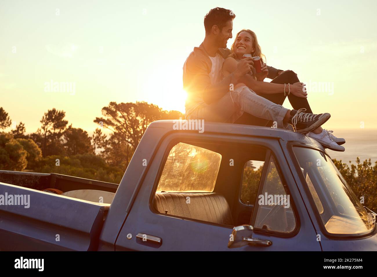 Hilltop romance at sunset. Shot of an affectionate young couple on a roadtrip. Stock Photo