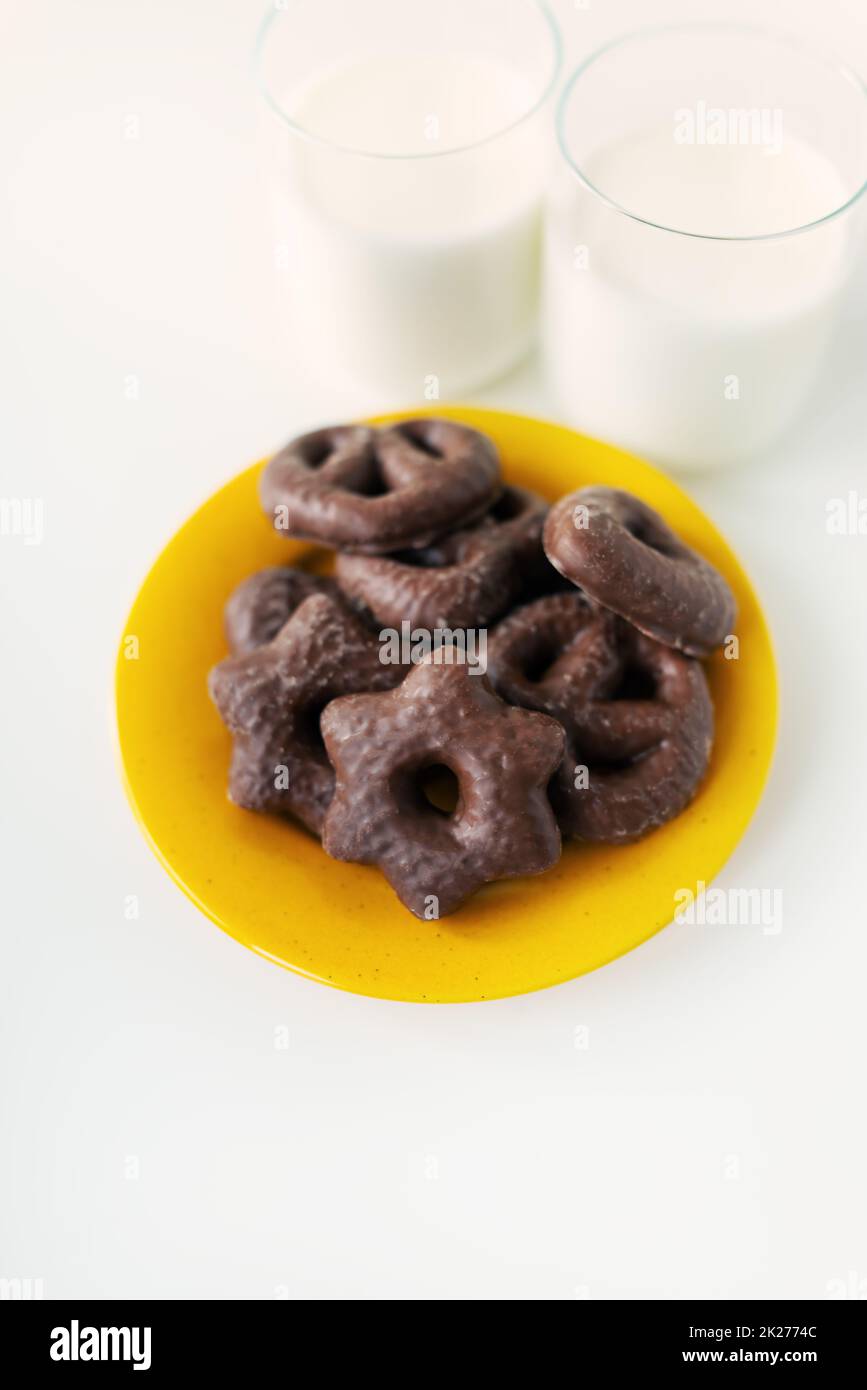 Chocolate covered gingerbread cookies lie on a yellow plate along with a glass of milk. Place for an inscription. Stock Photo