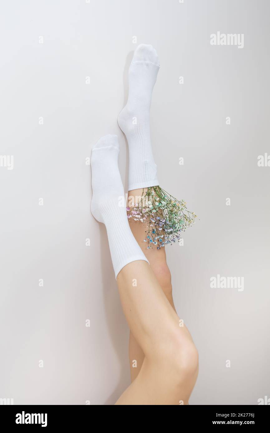 The legs of a girl in white socks in which there are flowers stand up. The concept of smooth and beautiful legs. Stock Photo