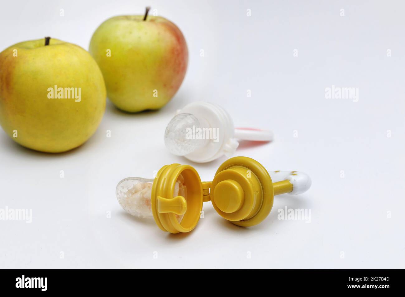 Nibblers with fresh apples on white table, closeup. Baby feeder. Stock Photo