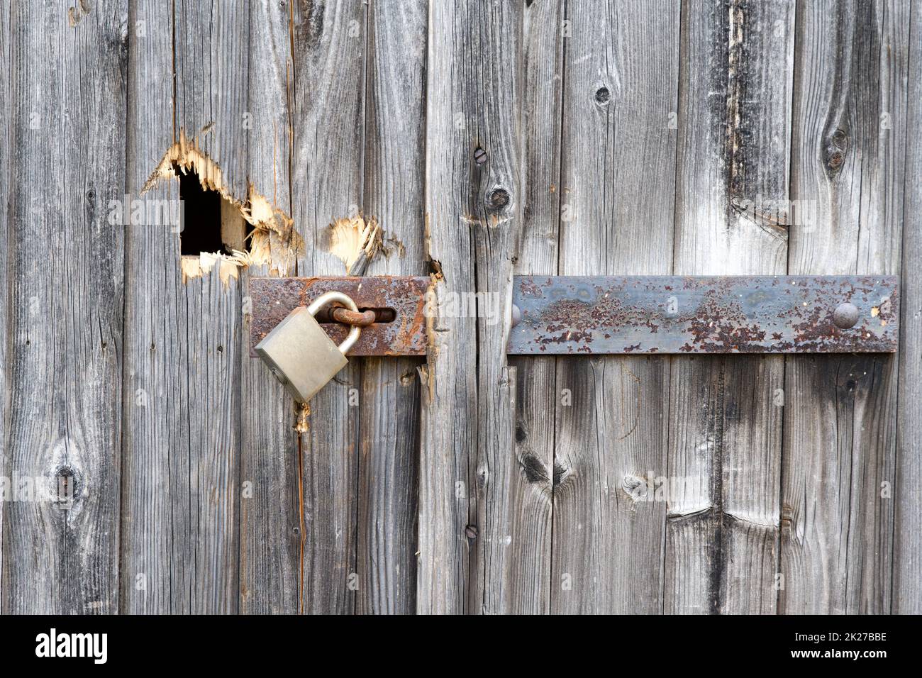old wooden gate with damages and rusty bolt and padlock Stock Photo