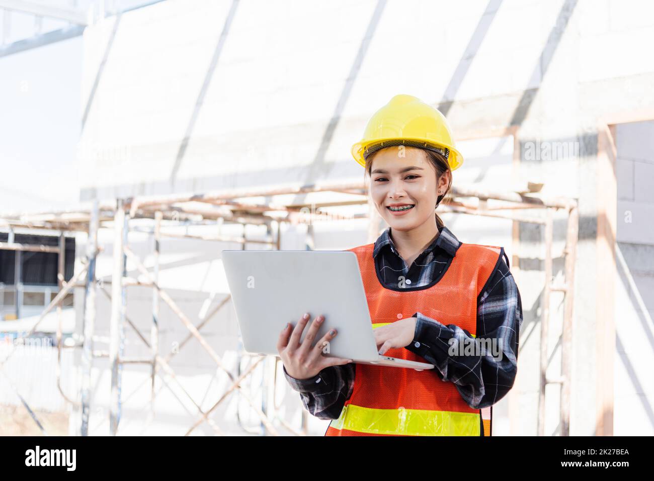 Asian engineer architect worker woman holding laptop inspect and oversee infrastructure progress at construction site Stock Photo