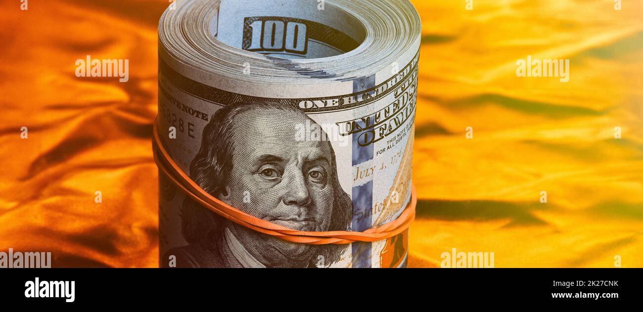 A roll of one hundred American dollars in close-up on a gold background. A big pile of cash dollars. One hundred dollar bills. Stock Photo