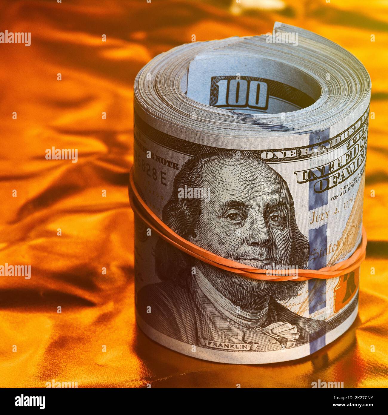 A roll of one hundred American dollars in close-up on a gold background. A big pile of cash dollars. One hundred dollar bills. Stock Photo