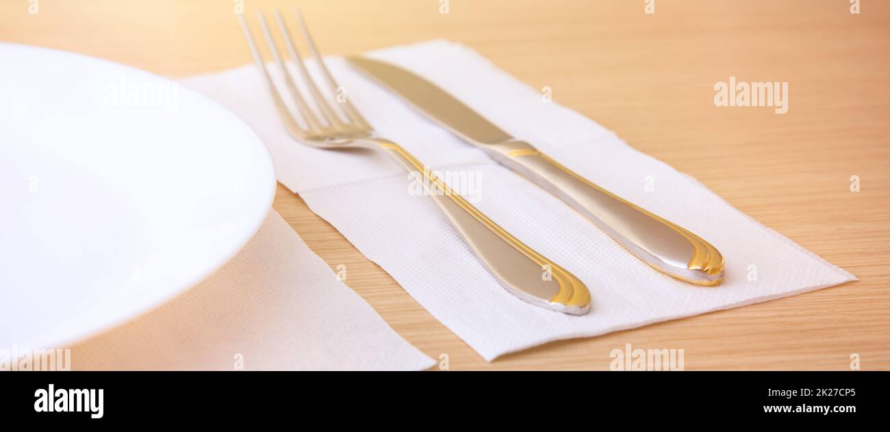 An empty plate, fork, knife, on a wooden table, side view. Stock Photo