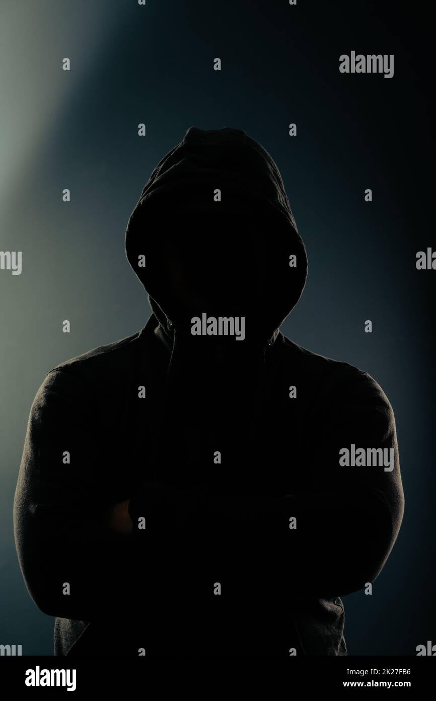 Mystery man with hidden face in a hood in the dark. Stock Photo