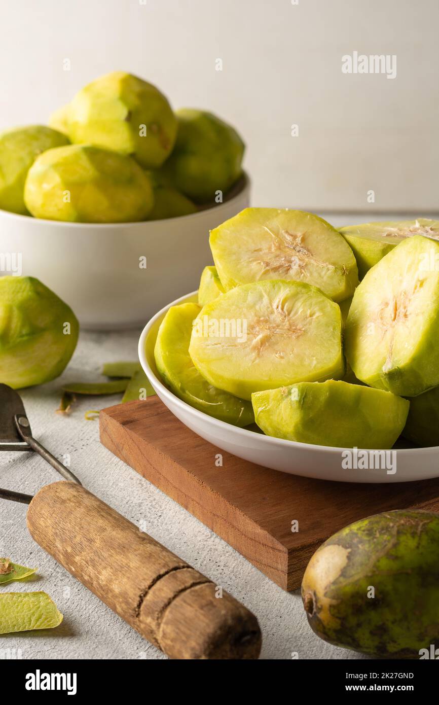 sliced ambarella or june plum on white textured surface, cut and peeled edible fruits in a bowl for making vegetarian condiment or sauce, soft-focus b Stock Photo
