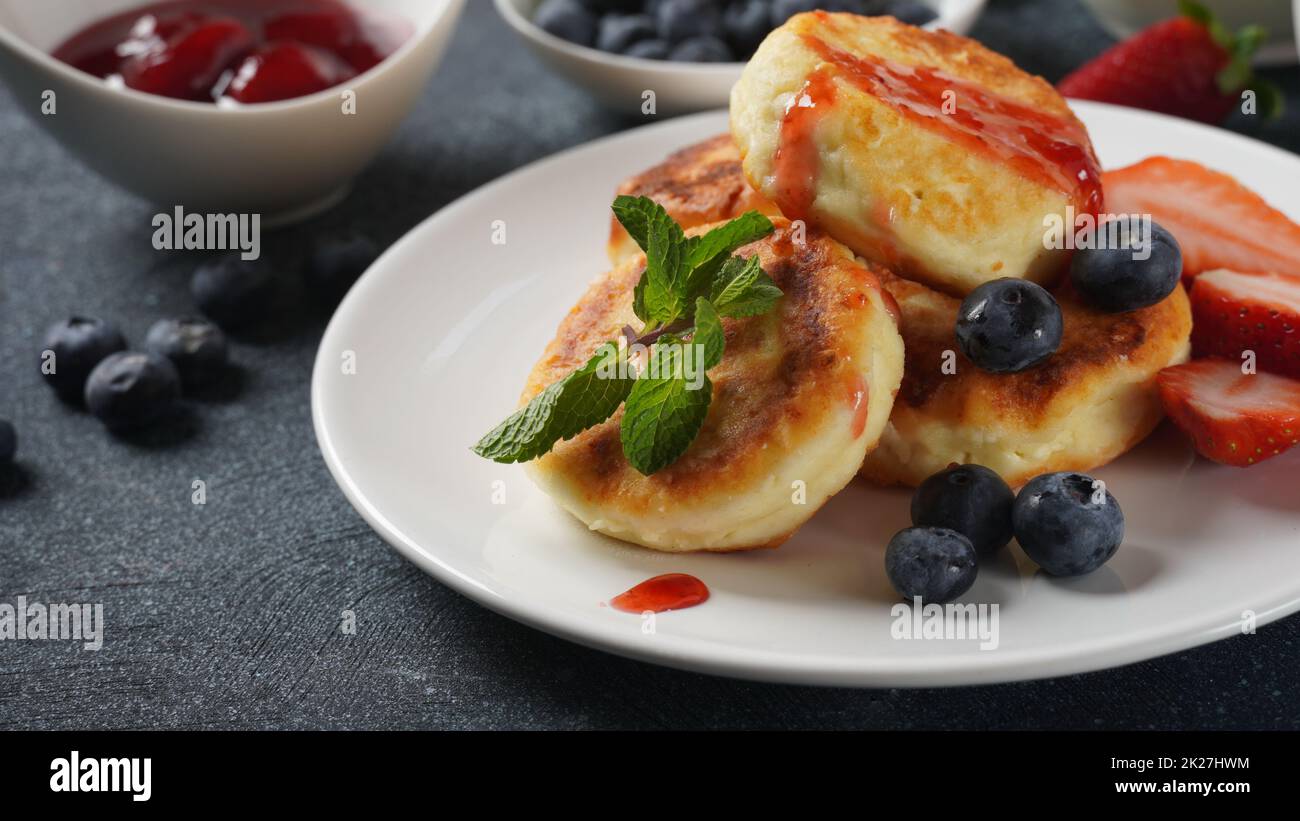 Cottage cheese fritters or syrniki or pancakes with fresh blueberries, strawberries and strawberry jam. Tasty dessert or sweet breakfast. Russian, Ukrainian cuisine Stock Photo