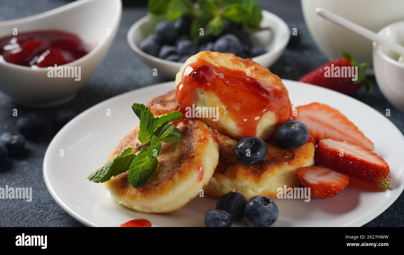 Cottage cheese fritters or syrniki or pancakes with fresh blueberries, strawberries and strawberry jam. Tasty dessert or sweet breakfast. Russian, Ukrainian cuisine Stock Photo