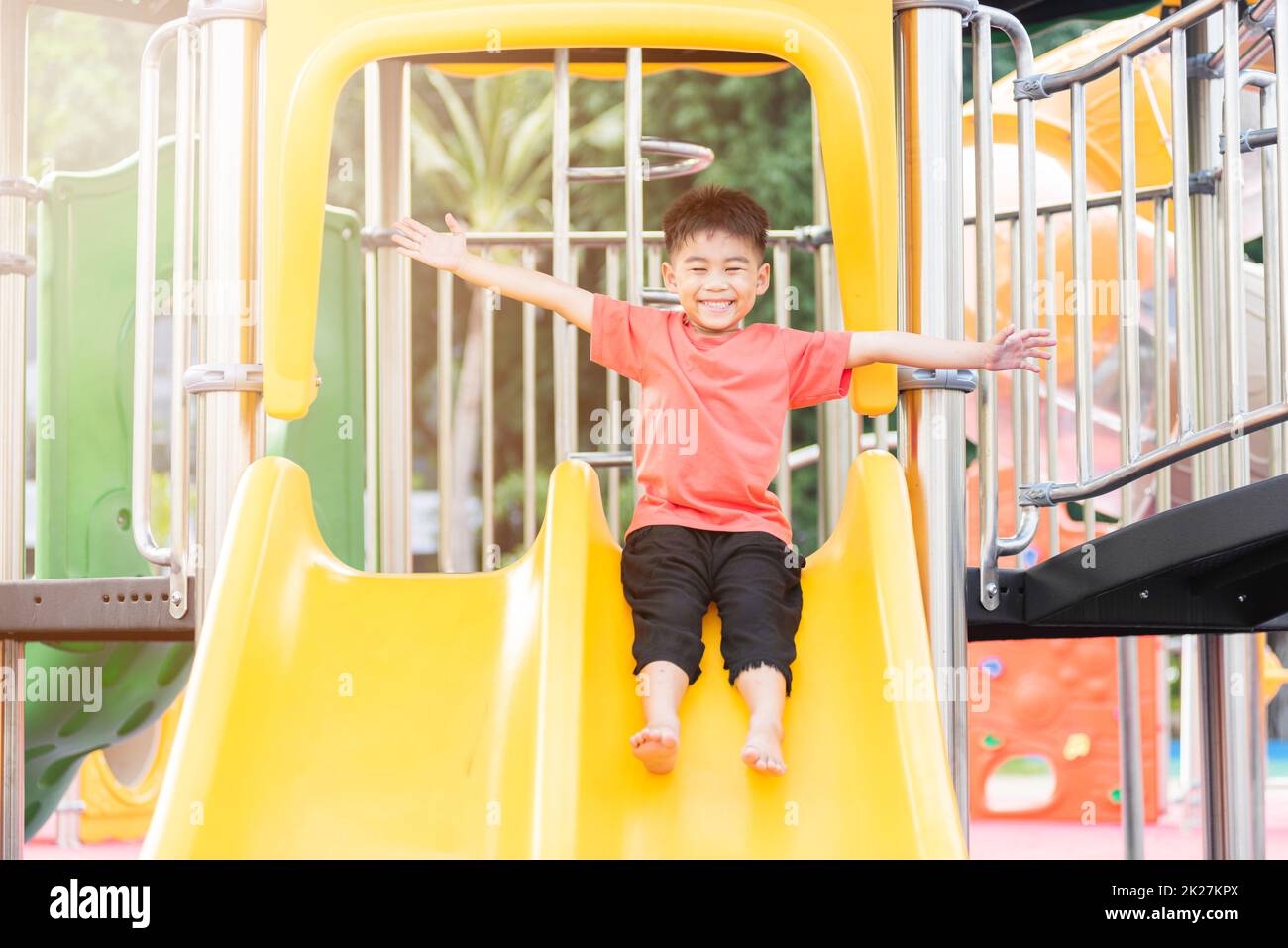 Asian child smiling playing on slider bar toy outdoor playground, happy preschool little kid having funny while playing on the playground equipment in the daytime in summer, Little boy climbing Stock Photo