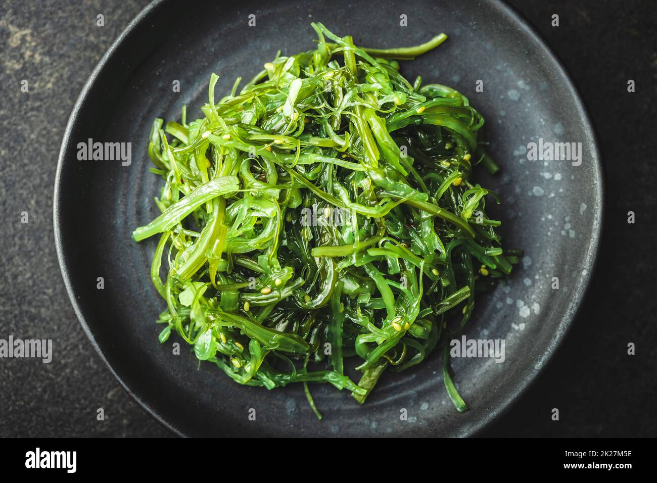 Green wakame. Seaweed salad on black plate. Stock Photo