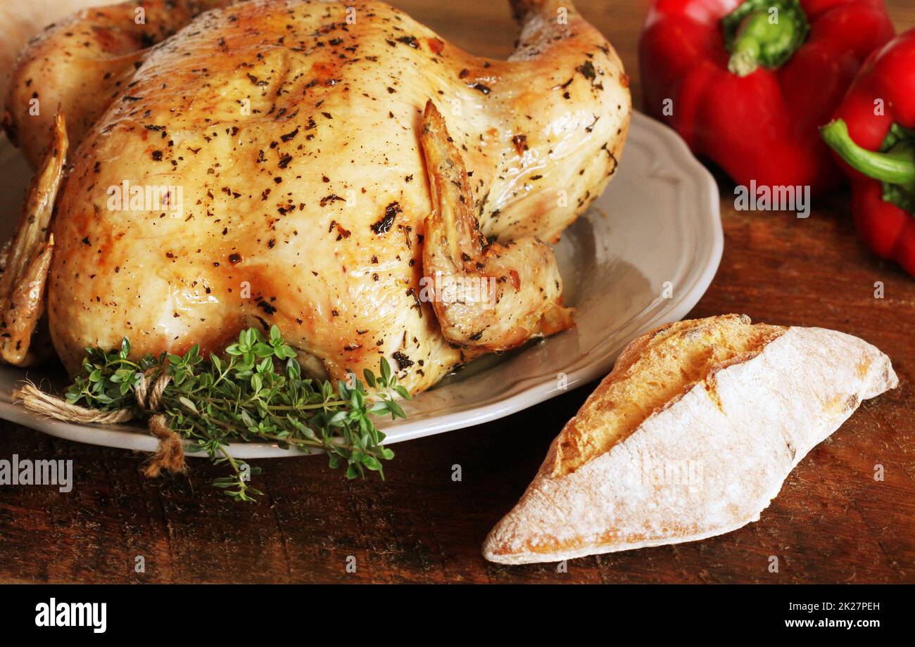 Whole roasted chicken with thyme, pepper and bread on wooden background Stock Photo