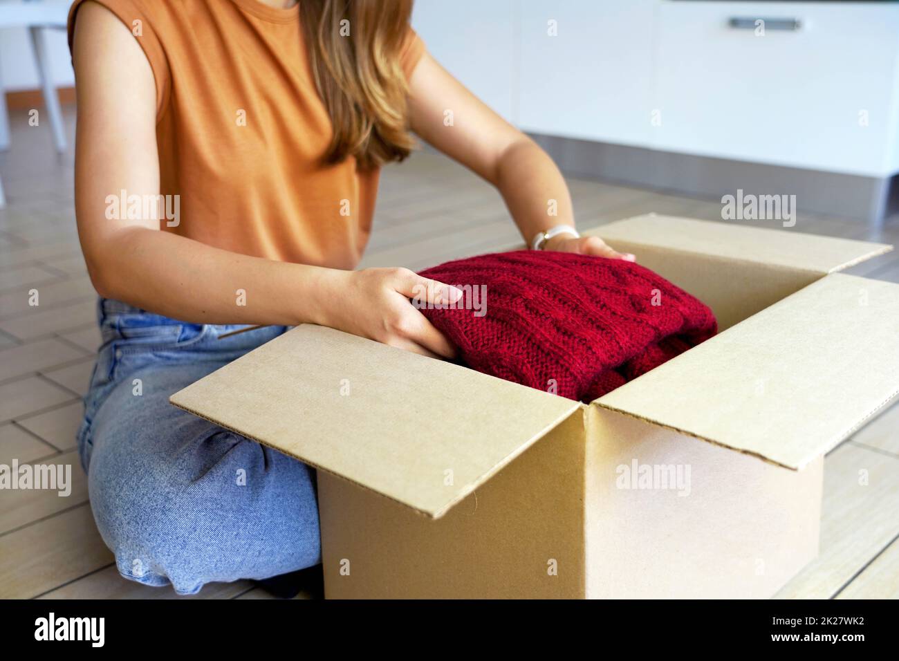 Second hand clothes. Beautiful young woman preparing donation box with clothing. Stock Photo