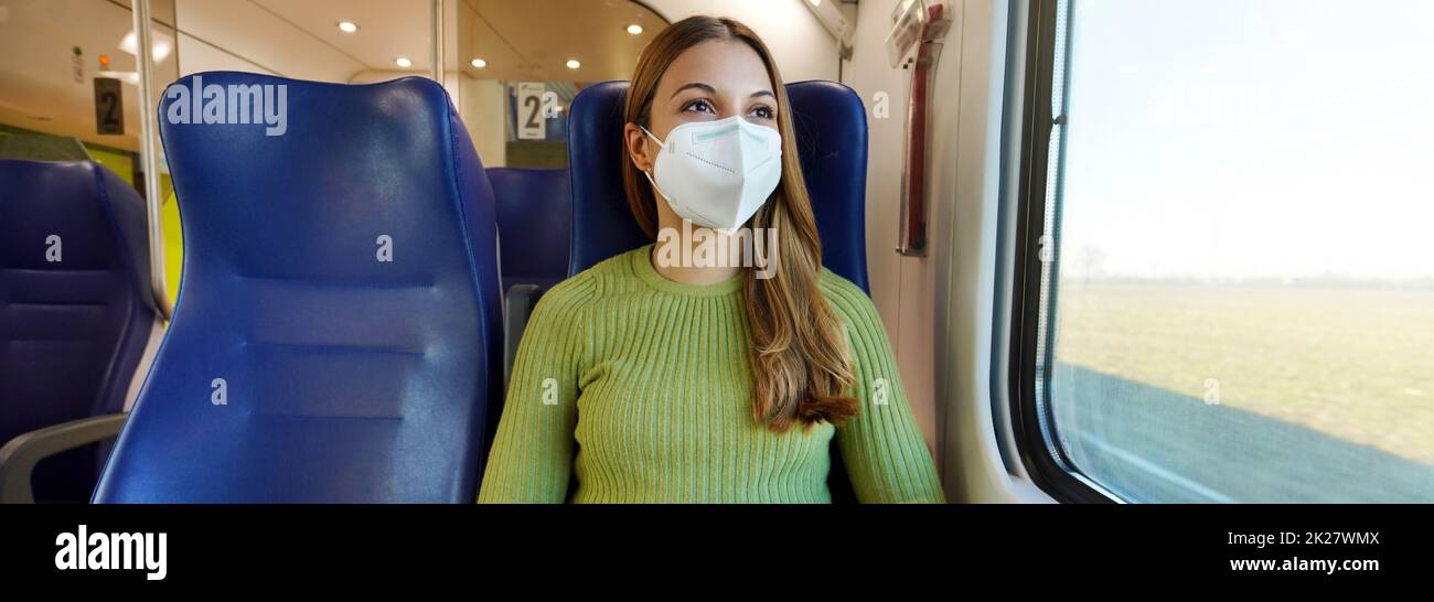 Banner of beautiful woman traveling on public transport wearing protective medical mask. Panoramic cropped photo of girl with face mask enjoying view through the window on train. Stock Photo