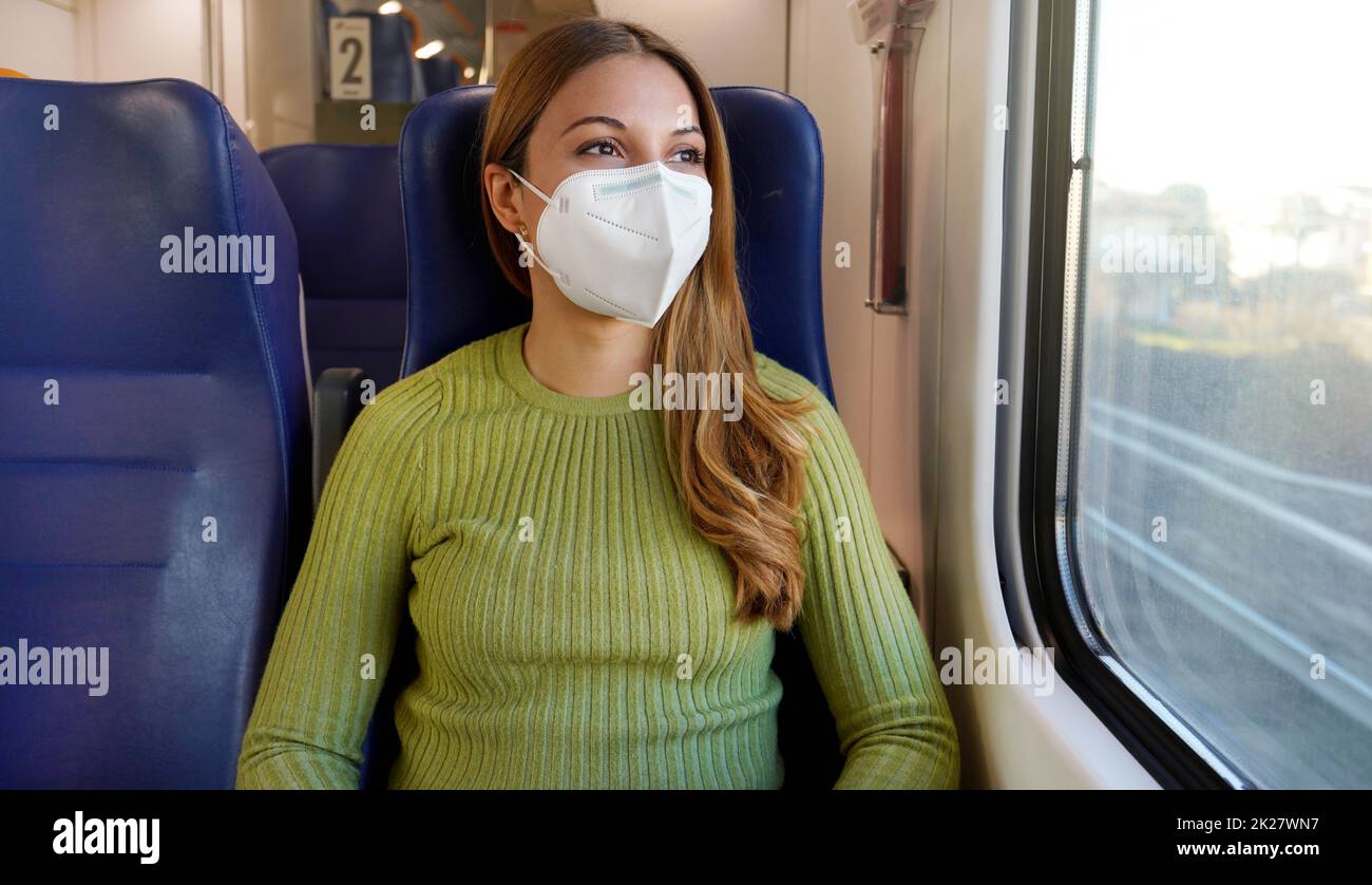 Portrait of woman traveling on public transport wearing protective medical mask. Banner cropped photo of girl with face mask enjoying view through the window on train. Stock Photo