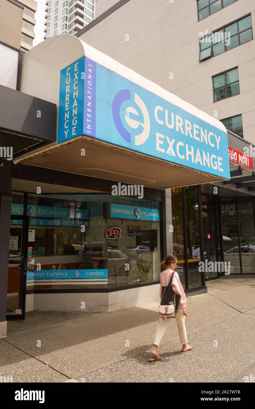 Stylishly dressed young woman walking past International Currency Exchange booth sign on Robson Street in downtown Vancouver, BC, Canada Stock Photo