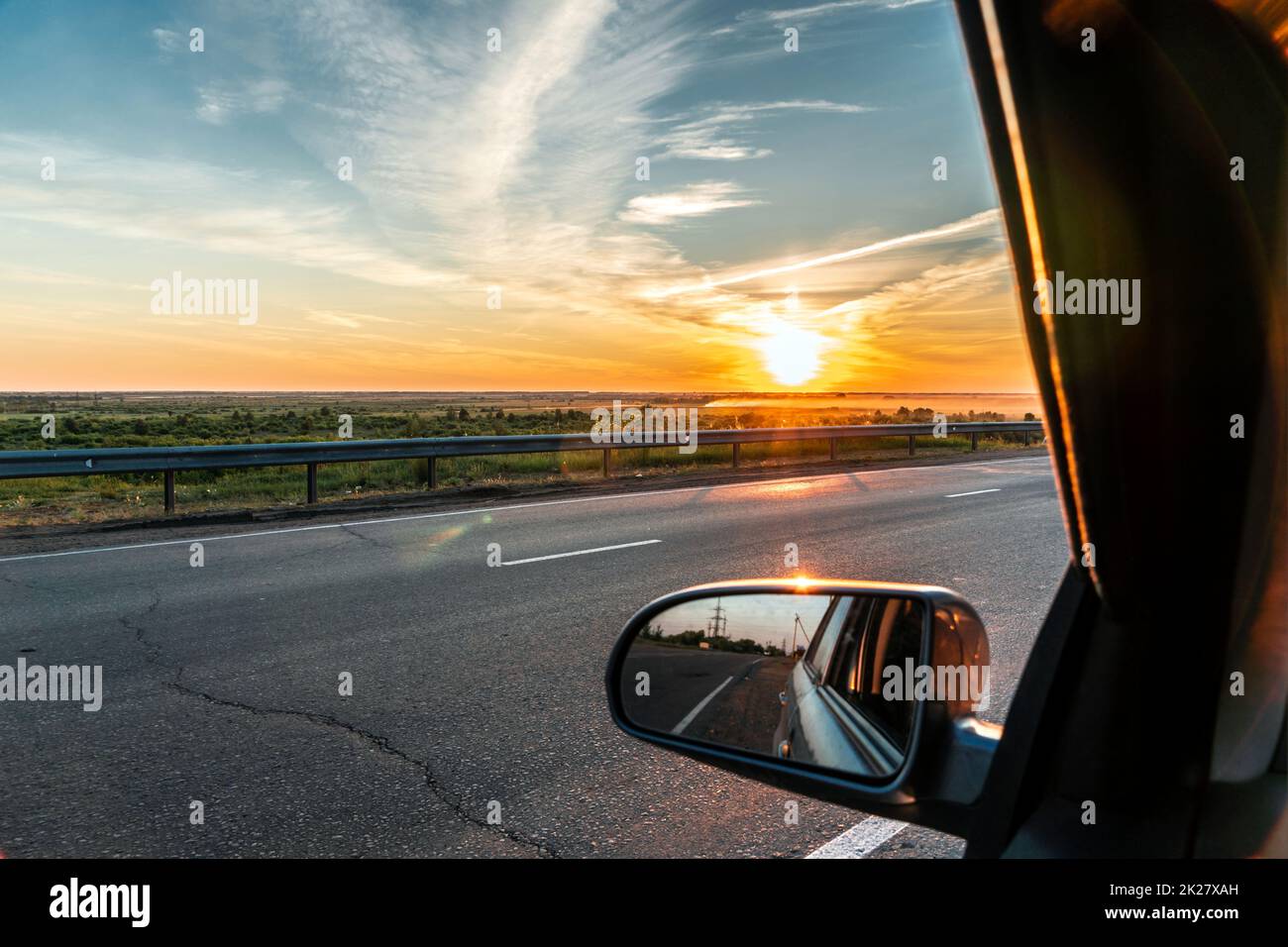 Evening trip to travel on the highway by car at sunset sunrise in the golden hour. Heavenly light.Dramatic evening sky with clouds and rays of the sun view from the window.Panoramic view of clouds Stock Photo