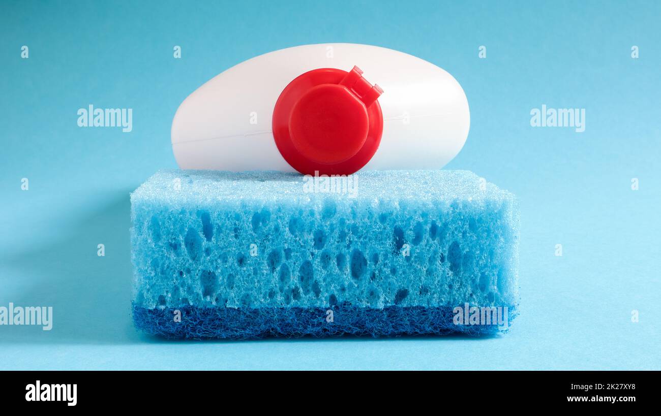 One blue sponge with a white bottle of detergent on a blue background. Convenience of sponges consists in good detergent retention that allows to use it economically Stock Photo