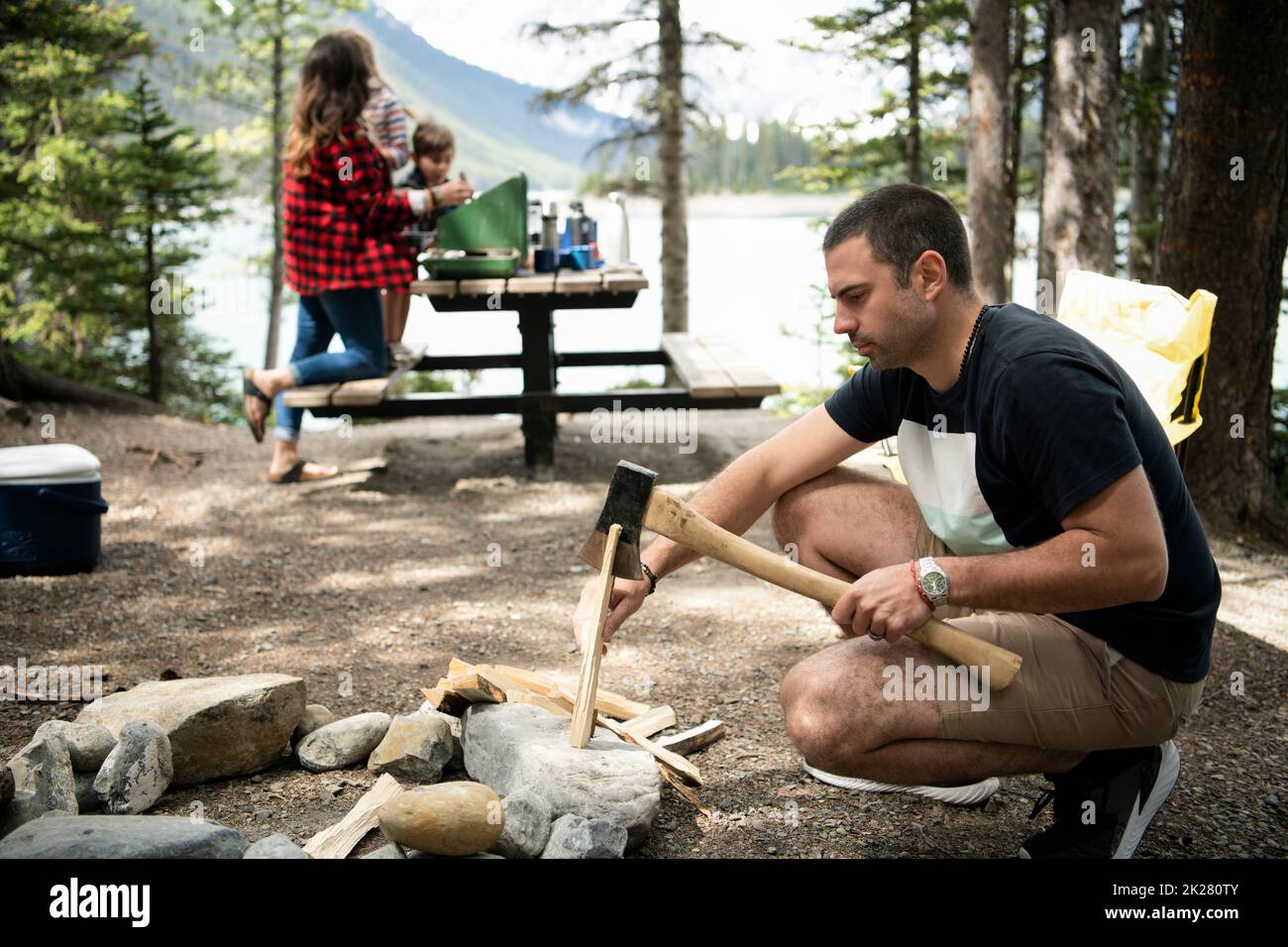 Man splitting firewood for campfire at campsite in woods Stock Photo