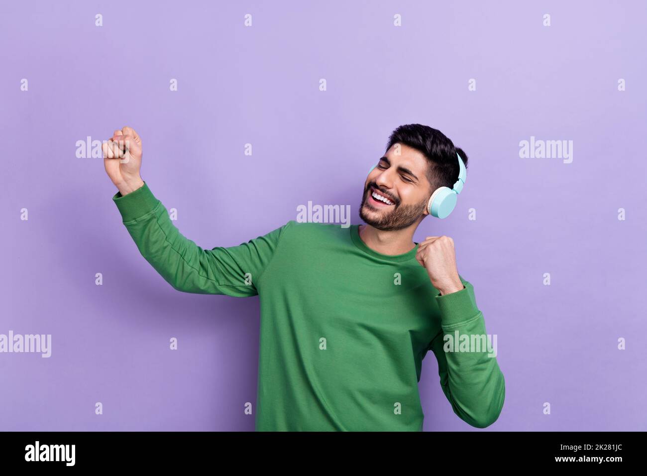 Photo of good mood cheerful guy green long sleeve headphones singing favorite artist dancing fists up isolated on violet color background Stock Photo