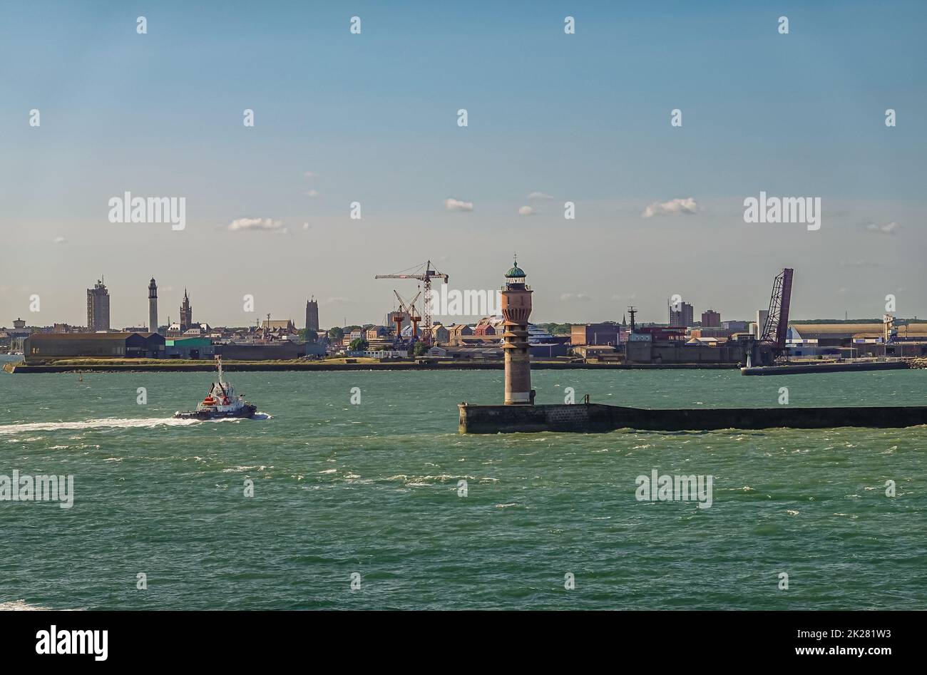 Europe, France, Dunkerque - July 9, 2022: Port scenery. Feu de Saint Pol light tower on its pier at entrance with city skyline on horizon. Belfry towe Stock Photo