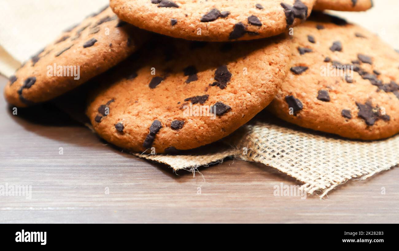 American chocolate chip cookies on a brown wooden table and on a linen napkin close-up. Traditional rounded crunchy dough with chocolate chips. Bakery. Delicious dessert, pastries. Rural still life. Stock Photo