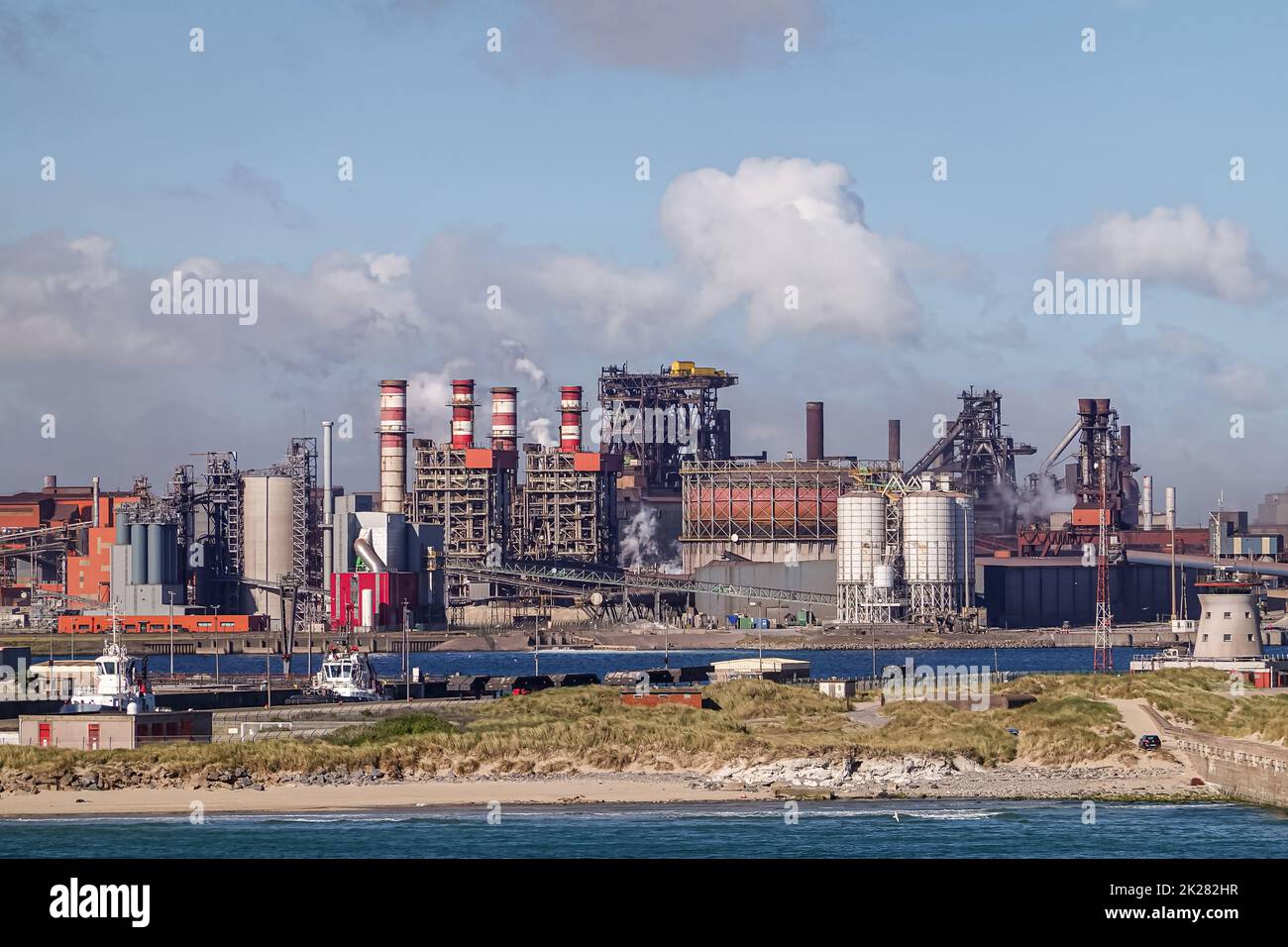 Europe, France, Dunkerque - July 9, 2022: Port scenery. Closeup of large power generation plant, based on coal and gas, under blue cloudscape, Cargo b Stock Photo