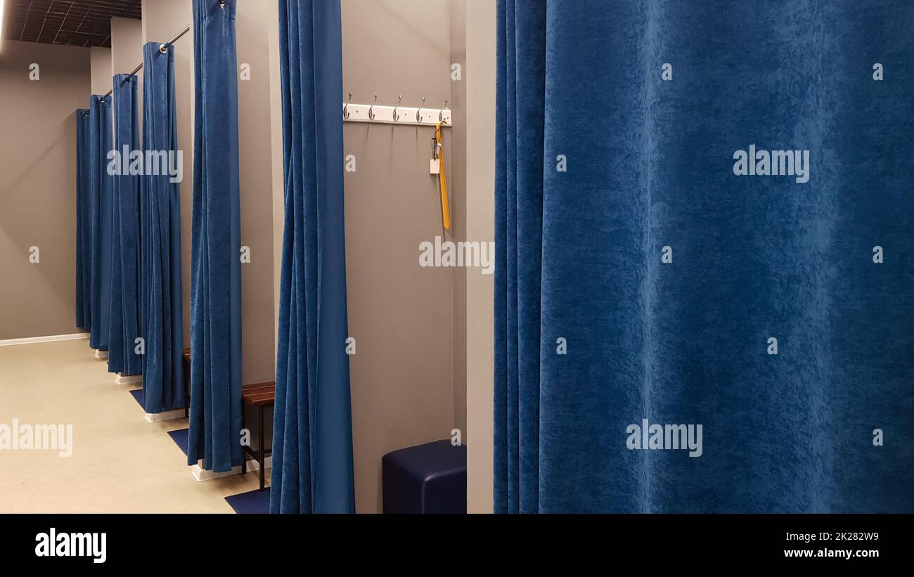 Boutique interior, fitting room in a shopping center. Nobody. Empty fitting rooms with blue curtains and gray walls and a large mirror. Dressing rooms in a clothing store without people. Stock Photo