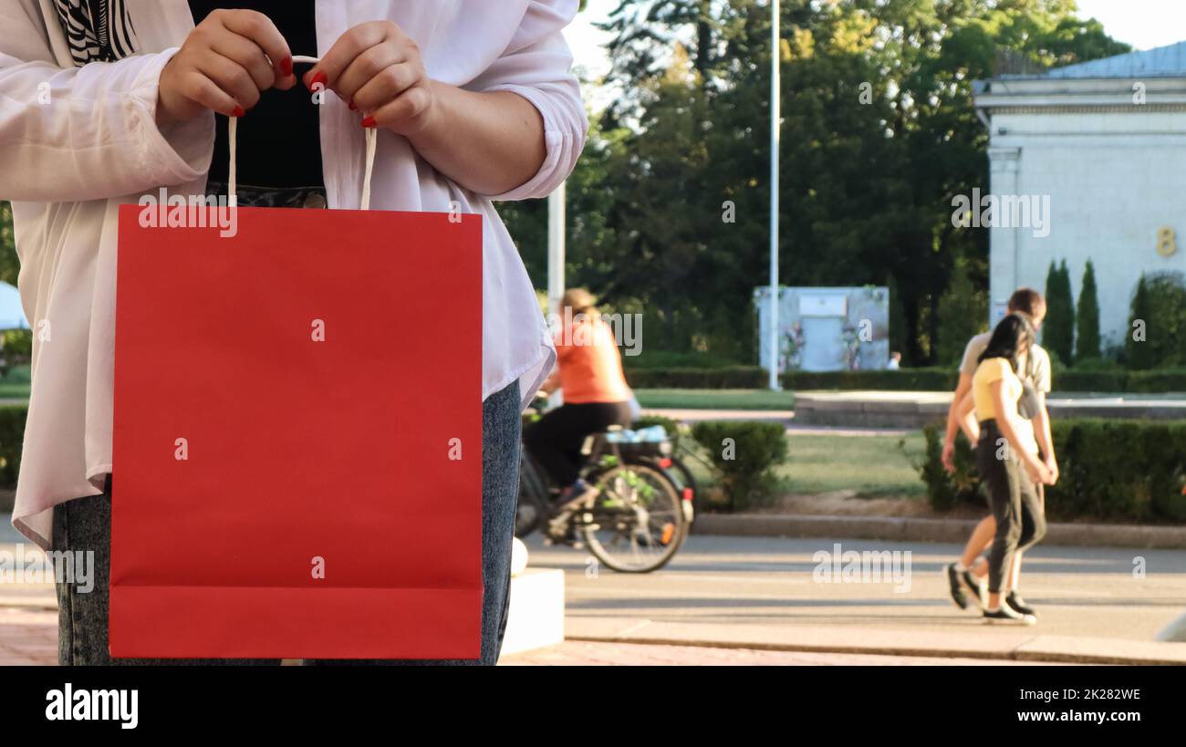 Close-up of a shopaholic woman with a red paper shopping bag in her hands. Crop the photo. Consumerism, shopping, lifestyle concept. Copy space for your logo. Black Friday Stock Photo