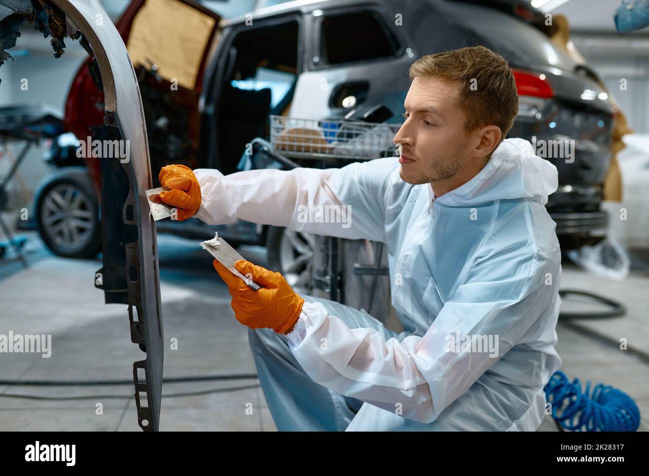 Mechanic puttying plastering car body in garage Stock Photo