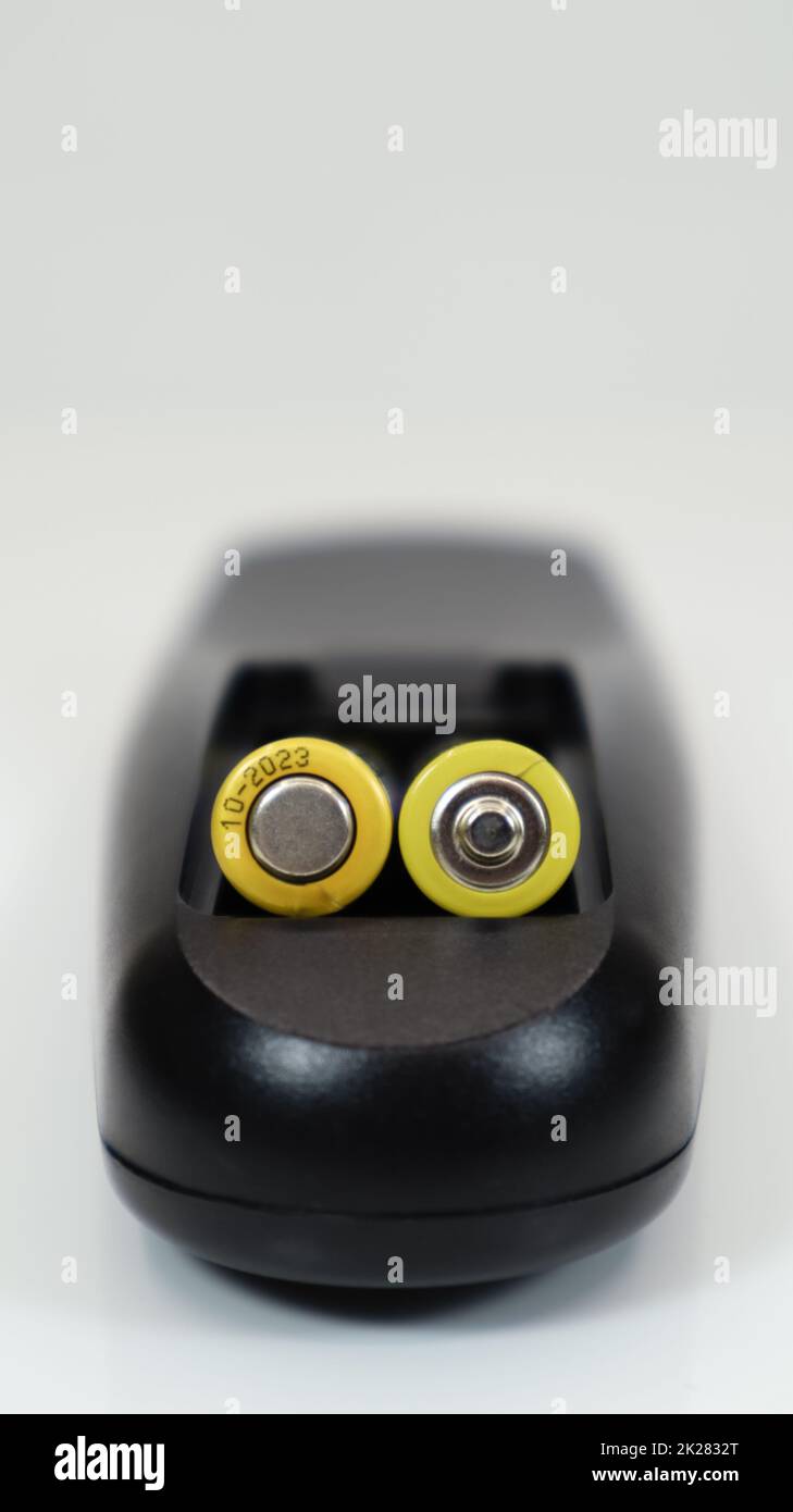 Black remote control with yellow AAA batteries on a white background