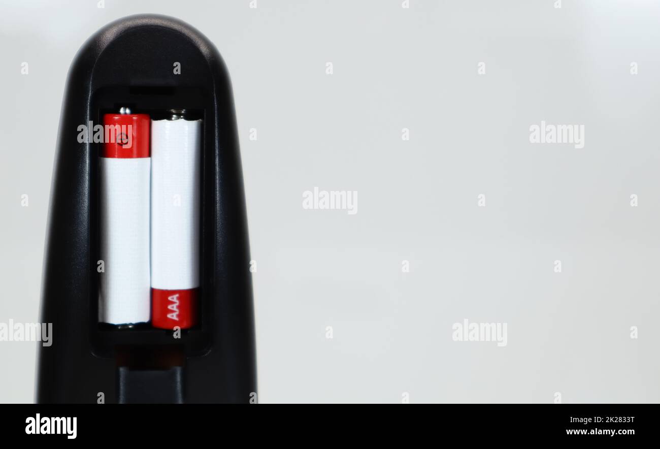 Black TV remote control with AAA alkaline batteries in red and white on a white background. Battery replacement, spare parts. Remote control battery compartment close-up. Copy space Stock Photo