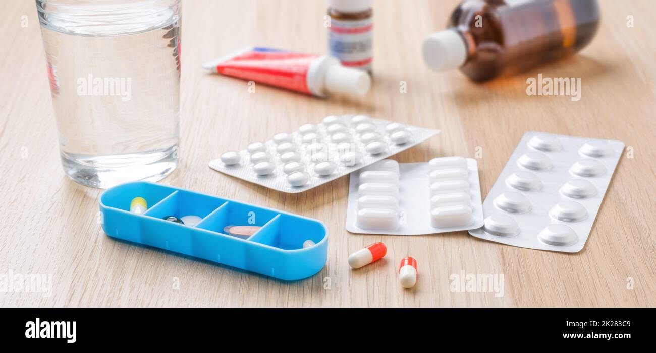 Different medicine pills and capsules with blister packs and a glass of