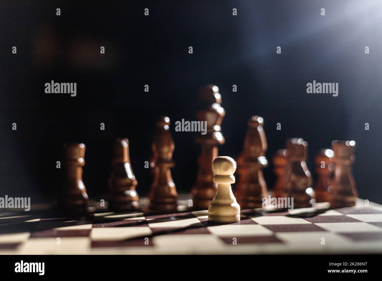 One pawn staying against full set of black chess pieces. One against all. Hero Stock Photo